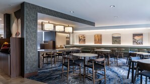 Um hall de hotel moderno com mesas redondas, cadeiras, área de bar e obras de arte nas paredes.