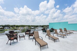 Eine Dachterrasse mit Liegestühlen und Korbstühlen mit Blick auf ein Gewässer und eine entfernte Küstenlinie.
