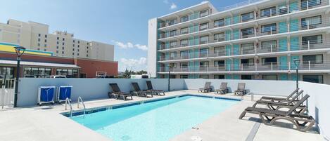 A rooftop pool area with lounge chairs, a pool, and a multi-story hotel building in the background.