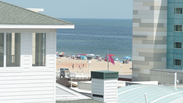 Blick auf einen Strand mit Sonnenschirmen und Menschen, ein Gebäude mit grüner Dachbegrünung und ein blaues Gebäude mit Fenstern.