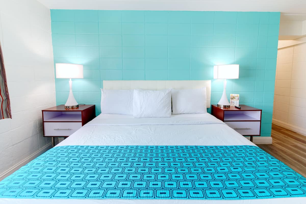 Une chambre d’hôtel avec un grand lit, deux tables de chevet et un mur d’accent de couleur turquoise.