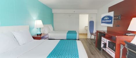 A hotel room with two beds, a desk, a microwave, and a television.