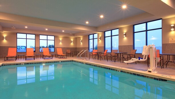 A pool area with chairs and tables, large windows, and a pool lift.