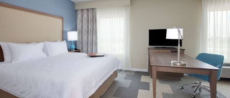 Une chambre d’hôtel avec un grand lit, un bureau avec un ordinateur, une télévision et une chaise.
