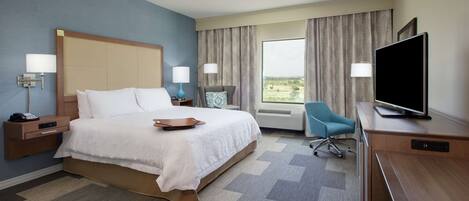 A hotel room with a bed, bedside tables, a desk with a television, a chair, and a large window with curtains.