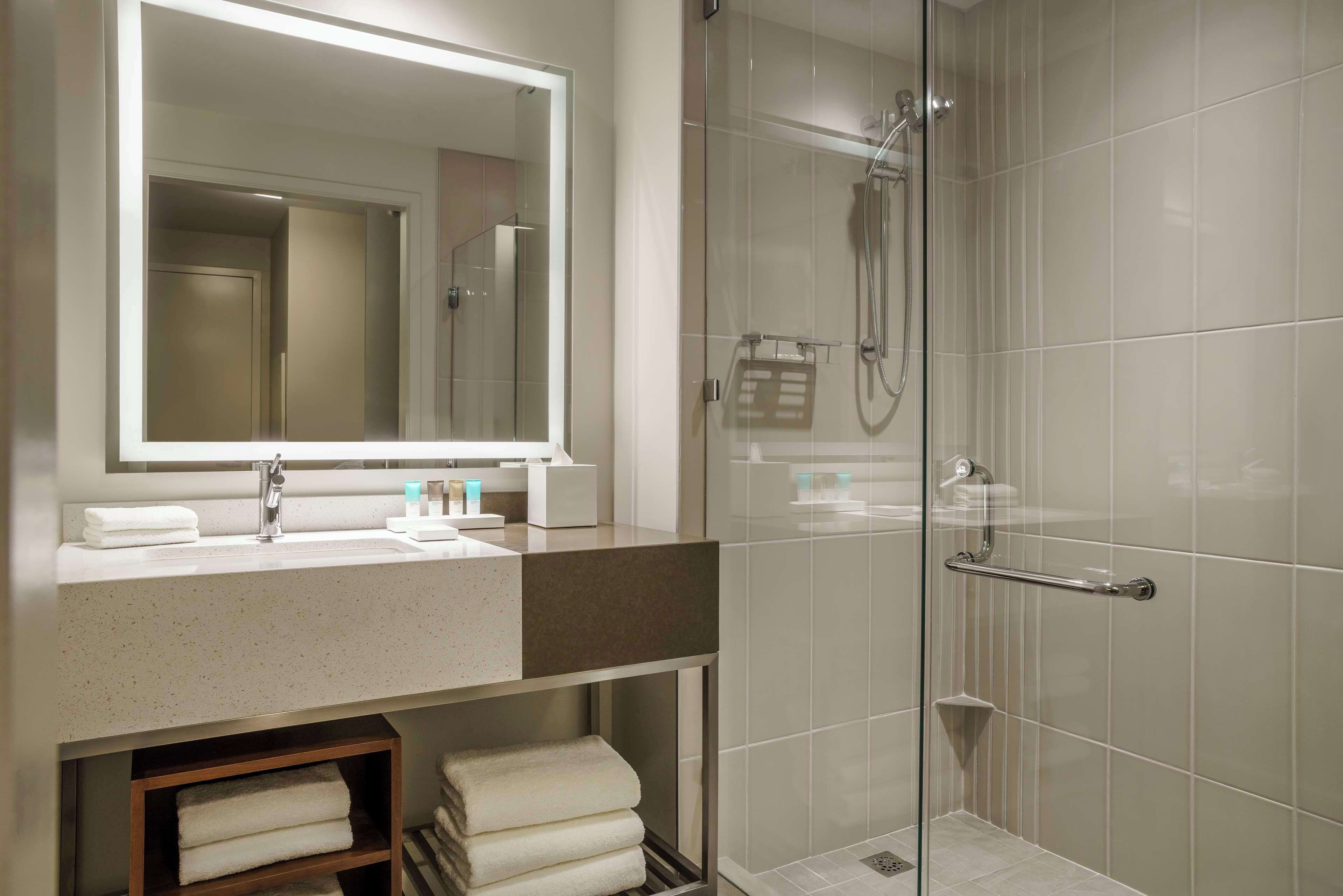 A modern bathroom with a glass shower enclosure, a large mirror, and a countertop with a sink and towel storage.