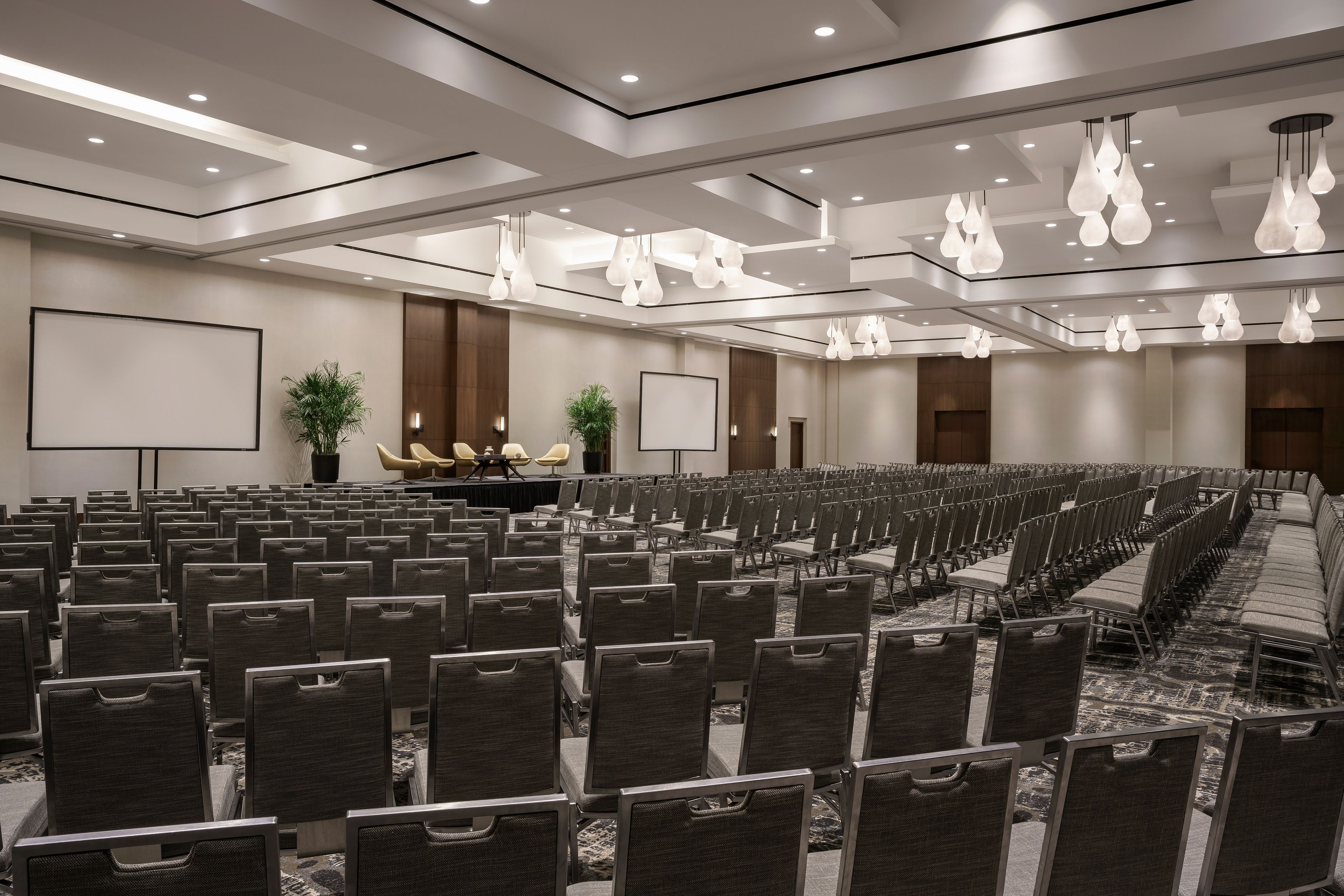 A conference room with rows of chairs, a stage with a podium, and a large screen.