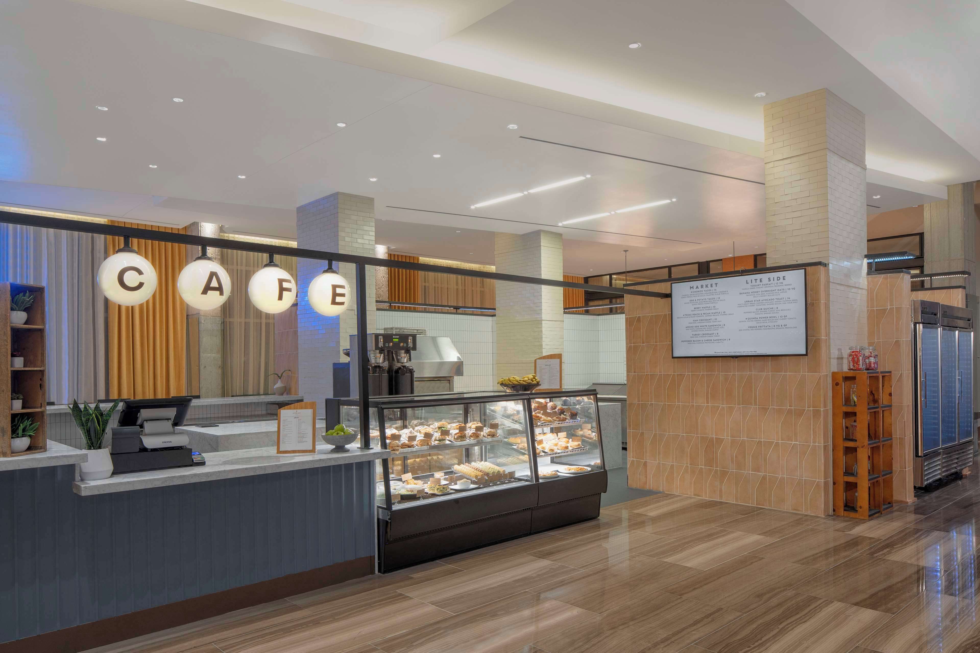 A modern cafe with a glass display case filled with pastries, a coffee machine, and a menu board.