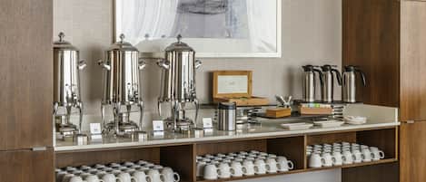 A breakfast bar with stainless steel appliances, a framed abstract painting, and neatly arranged white mugs.