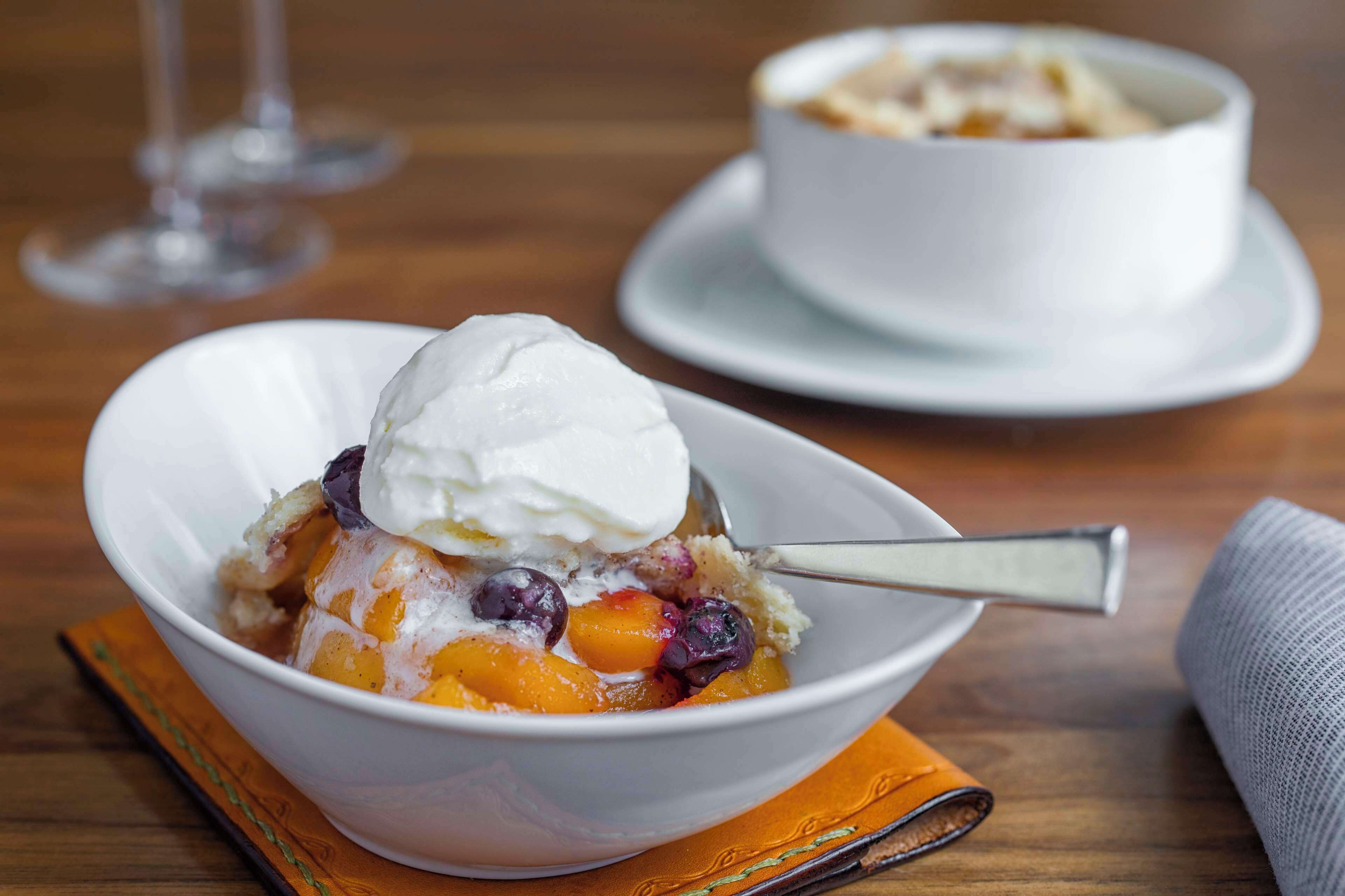 A bowl of dessert with fruit and a scoop of ice cream on a wooden table.