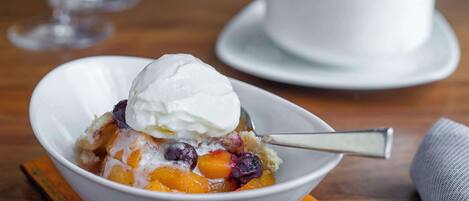A bowl of dessert with fruit and a scoop of ice cream on a wooden table.