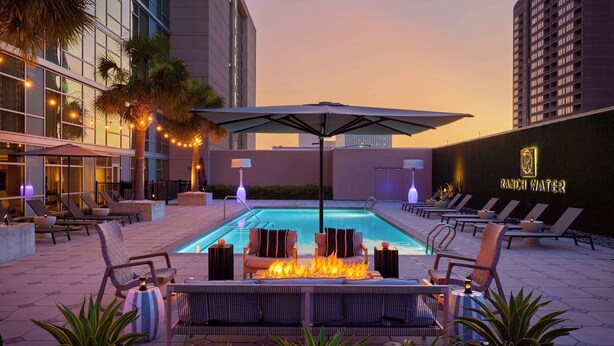 A rooftop pool area with lounge chairs, a fire feature, and a neon sign for "RANCH WATER".