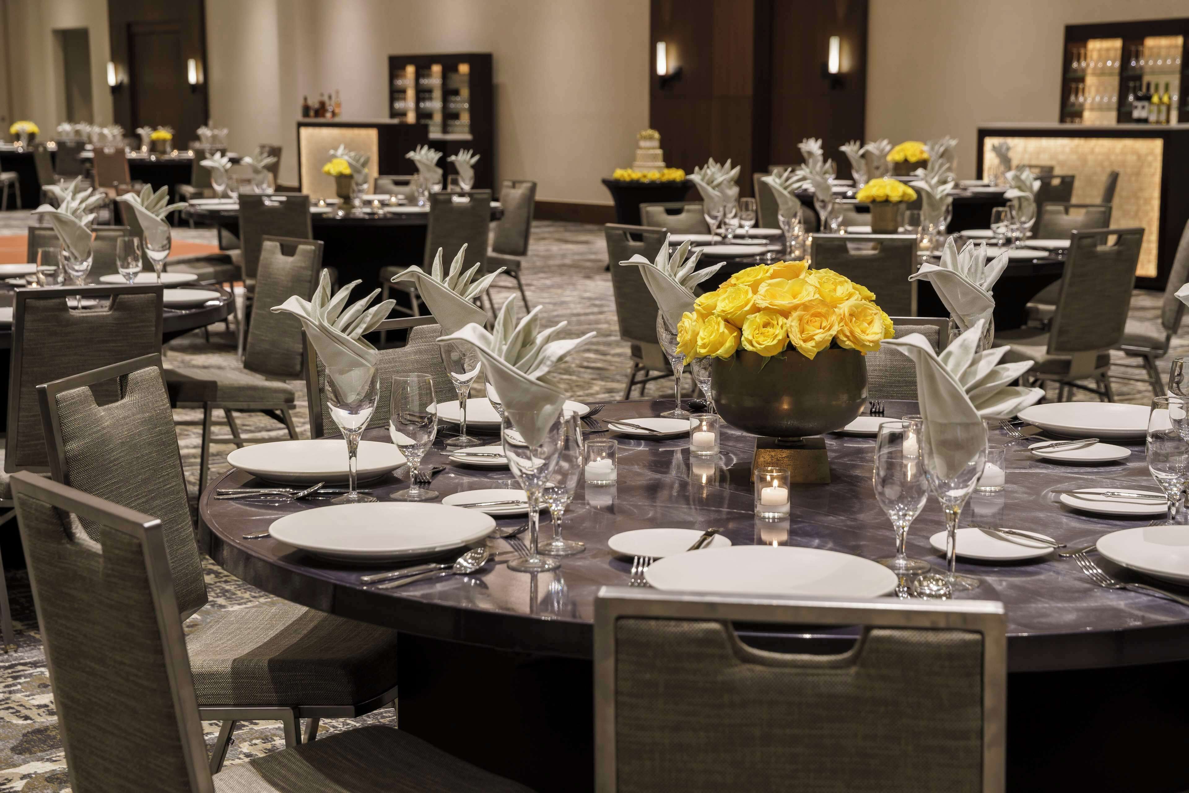 A well-set dining area with round tables, chairs, and centerpieces of yellow flowers.