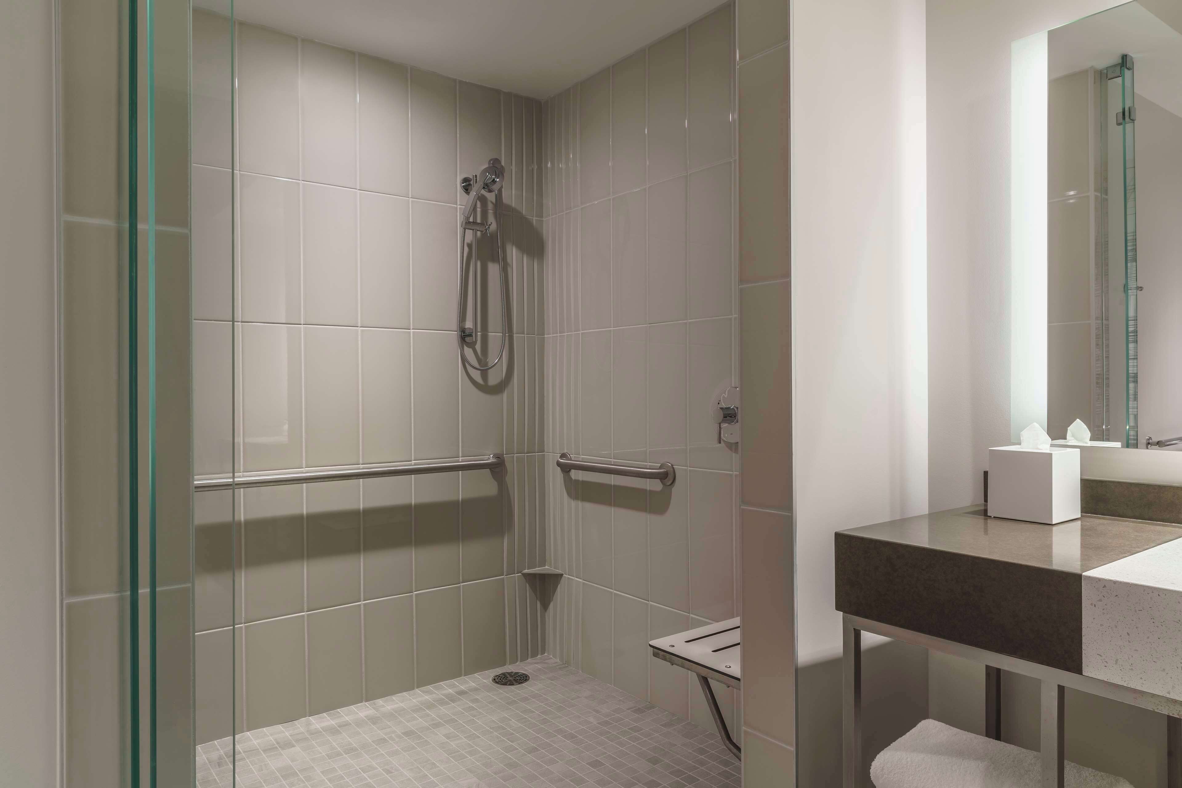 Un baño moderno con ducha envuelta en vidrio, tocador con encimera oscura y espejo sobre el lavabo.