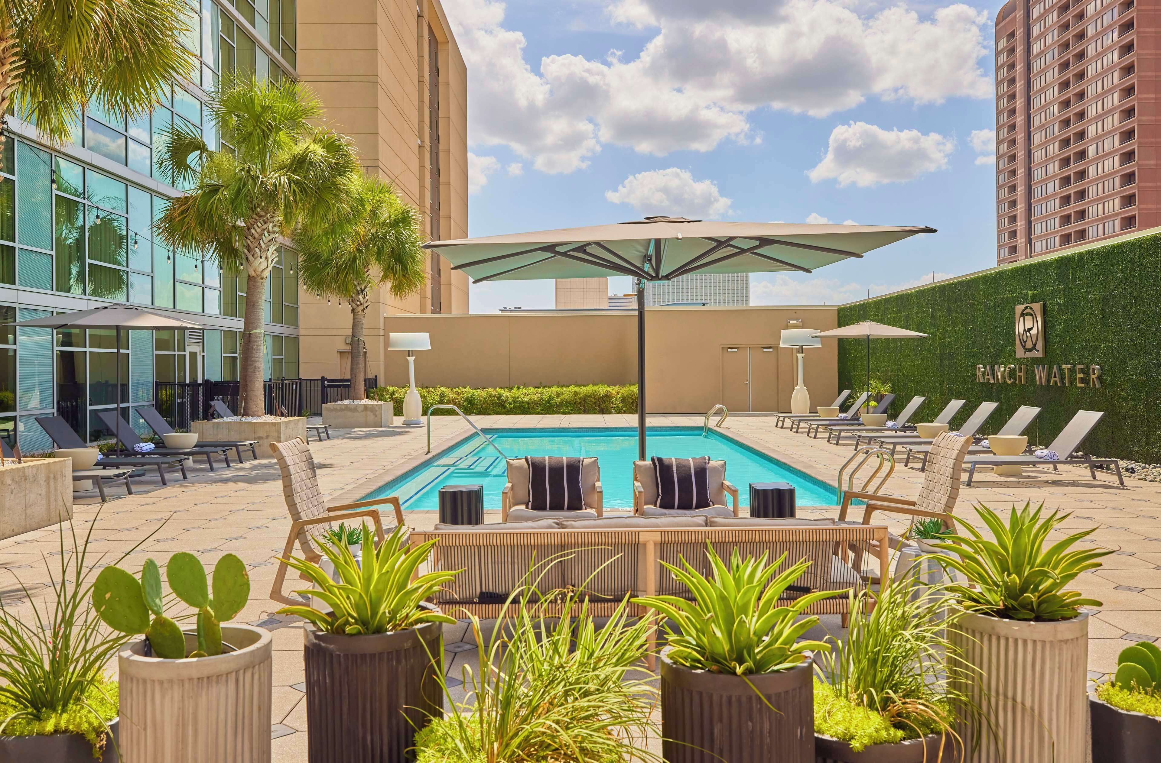 A rooftop pool area with lounge chairs, umbrellas, and potted plants.
