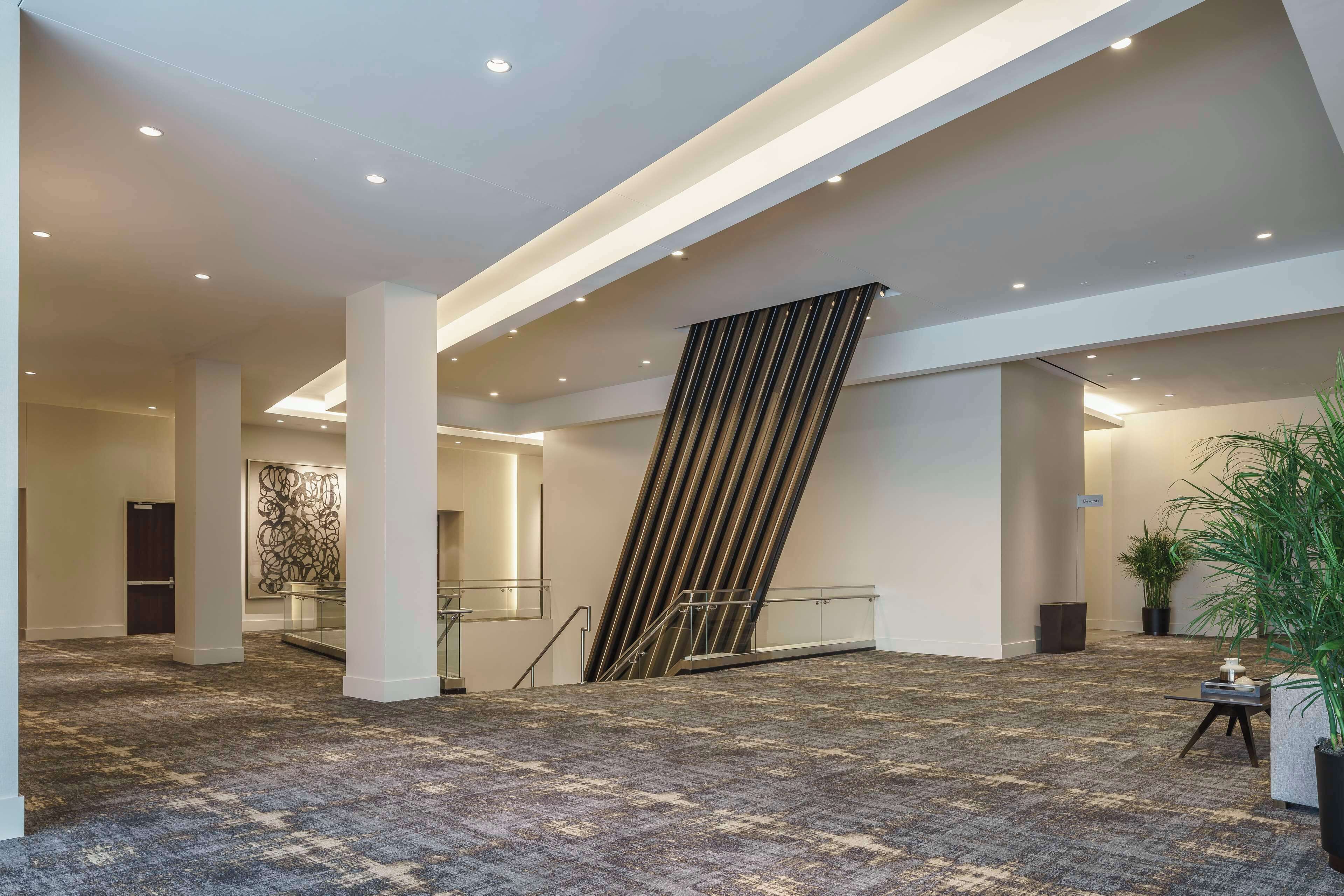 A spacious lobby with a patterned carpet, a staircase with a striped handrail, and a potted plant.