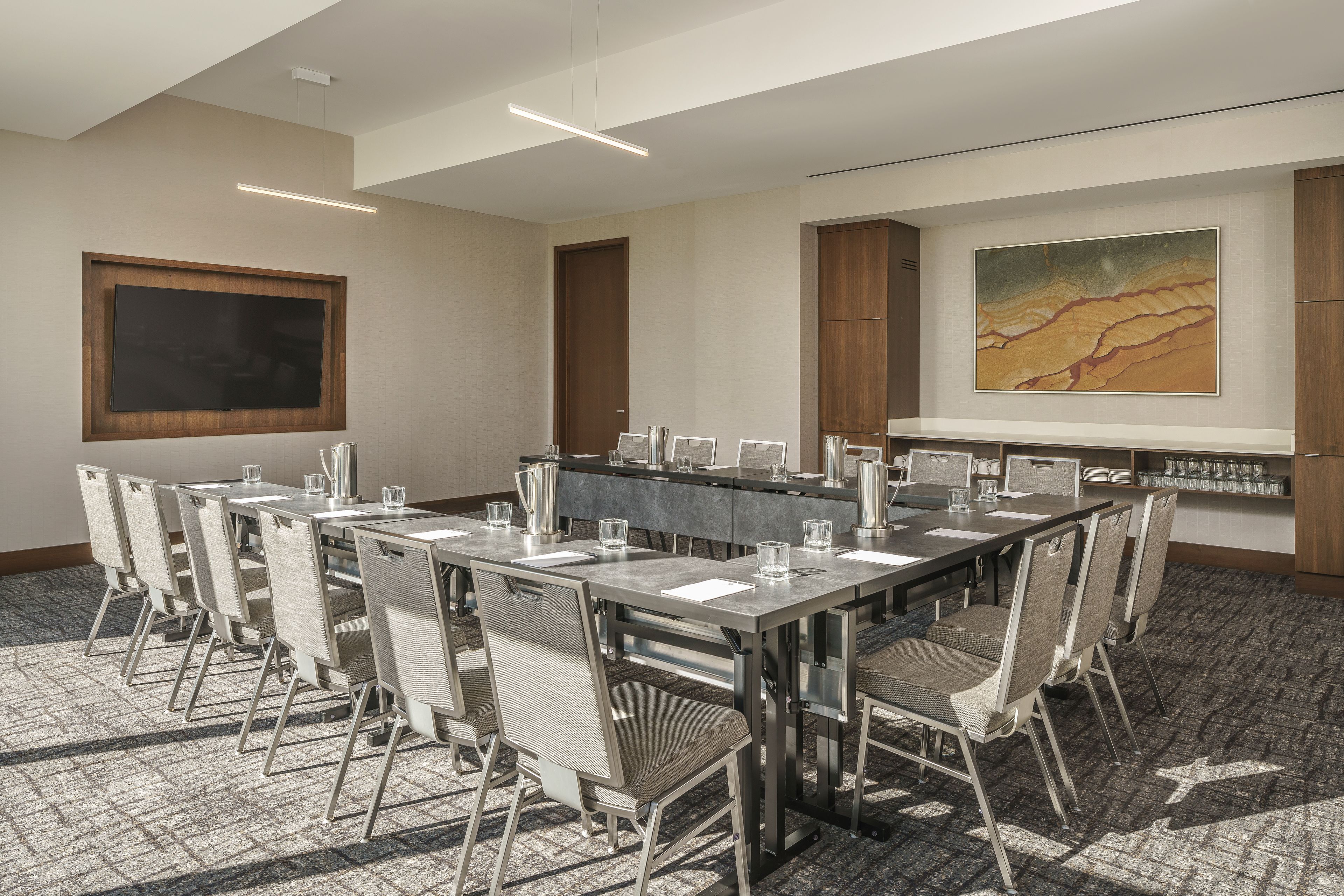 A conference room with a long table, chairs, a projector screen, and a painting on the wall.