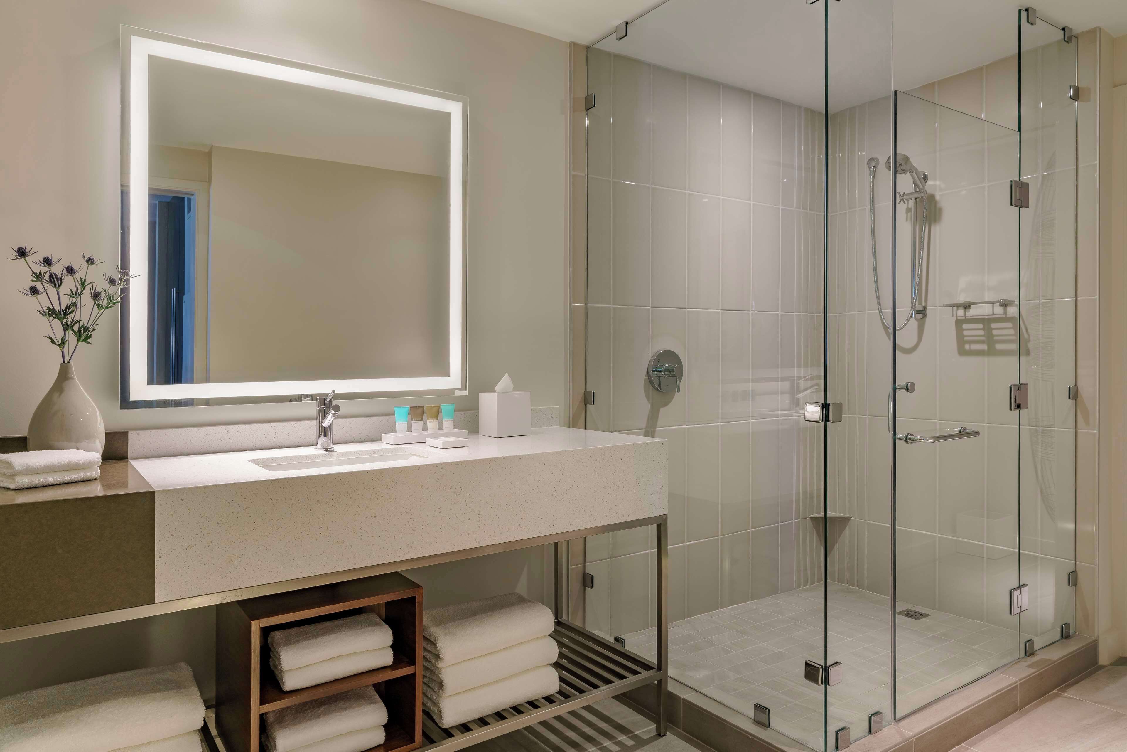 A modern bathroom with a glass-enclosed shower, a large mirror, and a vanity with towels.