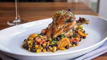 A plate of food with a roasted chicken leg, vegetables, and a glass of wine on a wooden table.