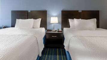 Een hotelkamer met twee bedden, een nachtkastje met een lamp en een blauw gestreept tapijt.
