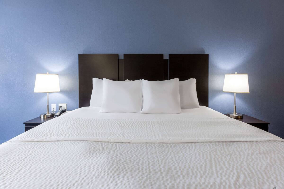 A neatly made bed with white linens and pillows, flanked by two bedside tables with lamps, against a blue wall.