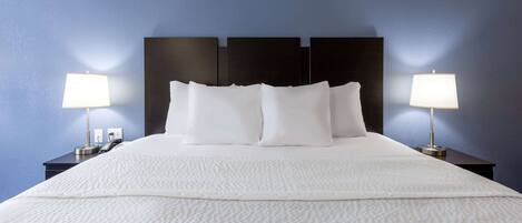 A neatly made bed with white linens and pillows, flanked by two bedside tables with lamps, against a blue wall.