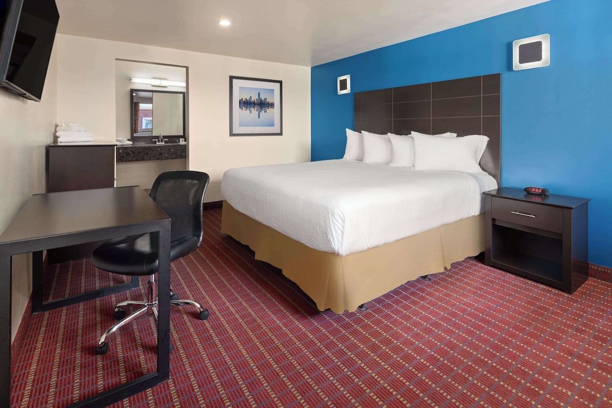 Une chambre d’hôtel équipée d’un lit, d’un bureau, d’une chaise et d’un téléviseur fixé au mur.