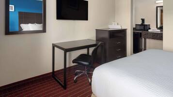Quarto de hotel com cama, escrivaninha, cadeira, televisão, micro-ondas e máquina de café.