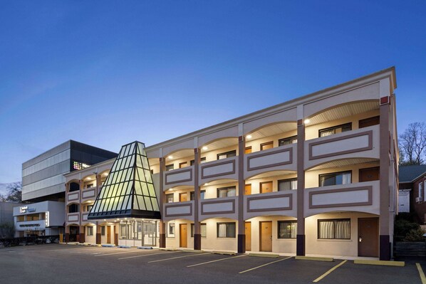 Um hotel com vários andares, átrio central, estacionamento e um edifício moderno adjacente.