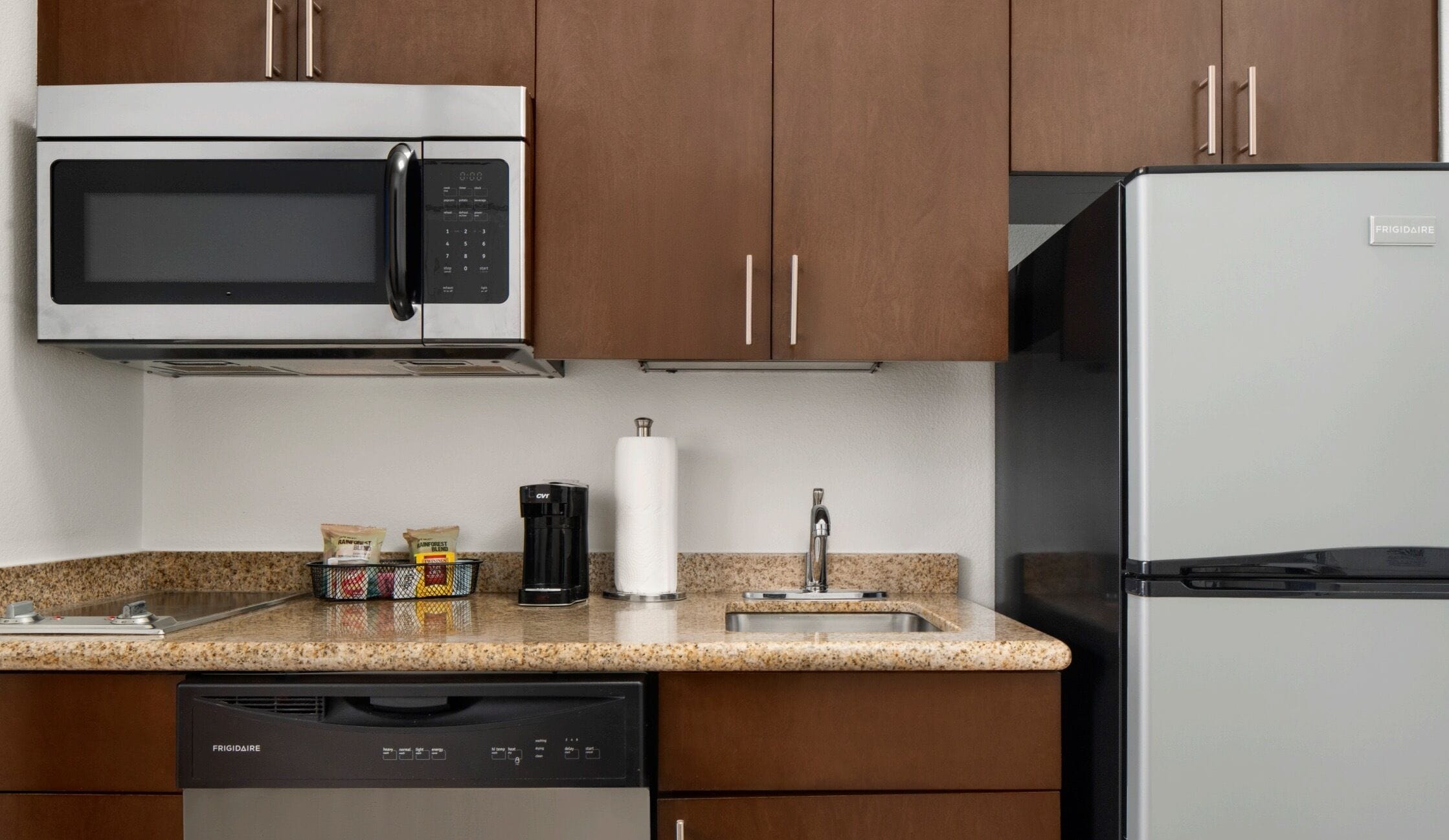 Cozinha equipada com micro-ondas, frigorífico e máquina de lavar loiça.
