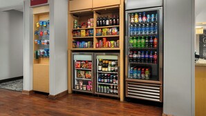 A self-service beverage station with refrigerated and non-refrigerated drink options, snack shelves, and a sign indicating the location. - TownePlace Suites by Marriott Florence (Florence)