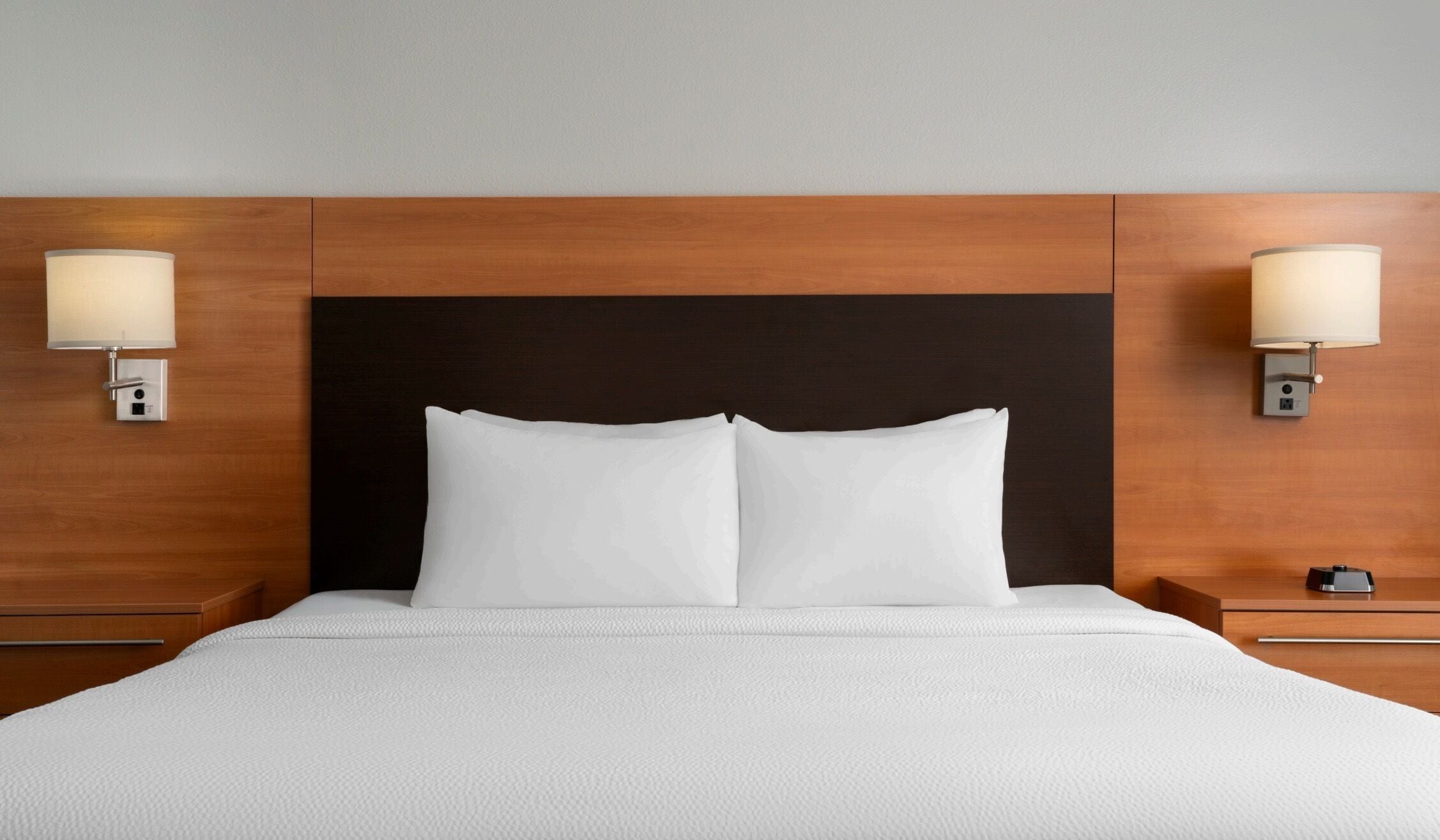 A hotel room with a large bed, two bedside tables, and wall-mounted lamps.