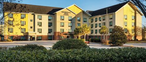 A multi-story hotel with a yellow and beige facade, multiple windows, and a parking lot in front.