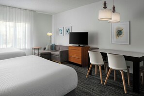 Een hotelkamer met twee bedden, een bureau met stoelen, een televisie en kunstwerken aan de muren.