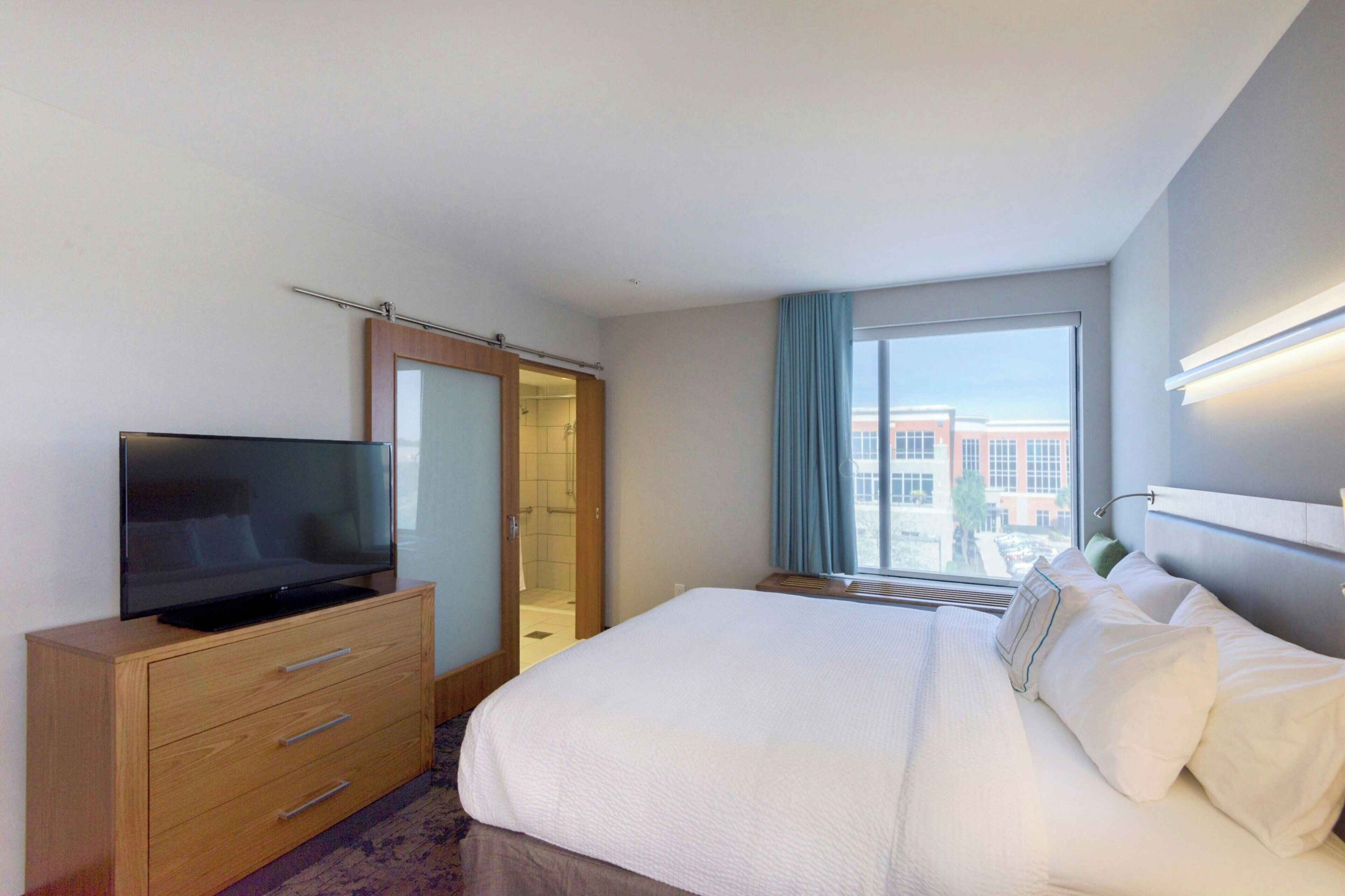 Een hotelkamer met een bed, een televisie op een houten dressoir, een inloopkast en een raam met uitzicht op gebouwen.