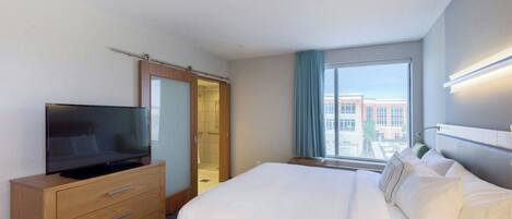 Une chambre d’hôtel avec un lit, un téléviseur posé sur une commode en bois, un dressing et une fenêtre donnant sur des immeubles.