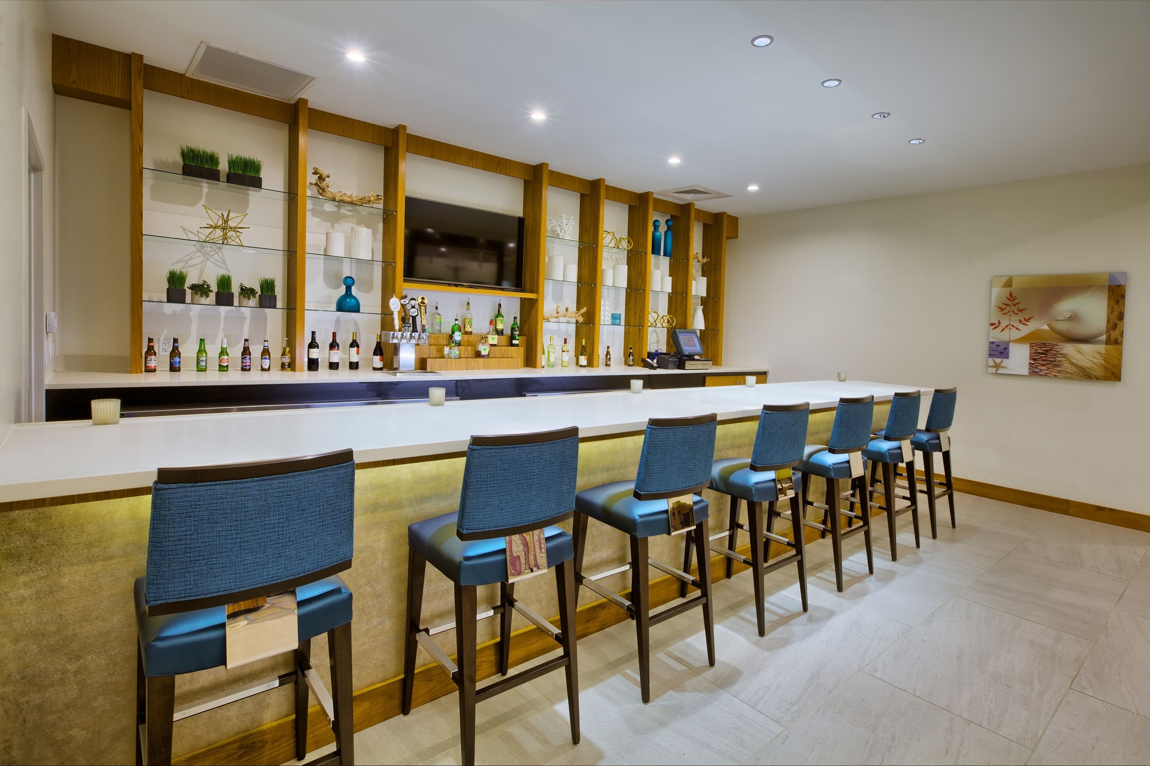 A bar area with a long counter, multiple chairs, and shelves with bottles and decorative items.