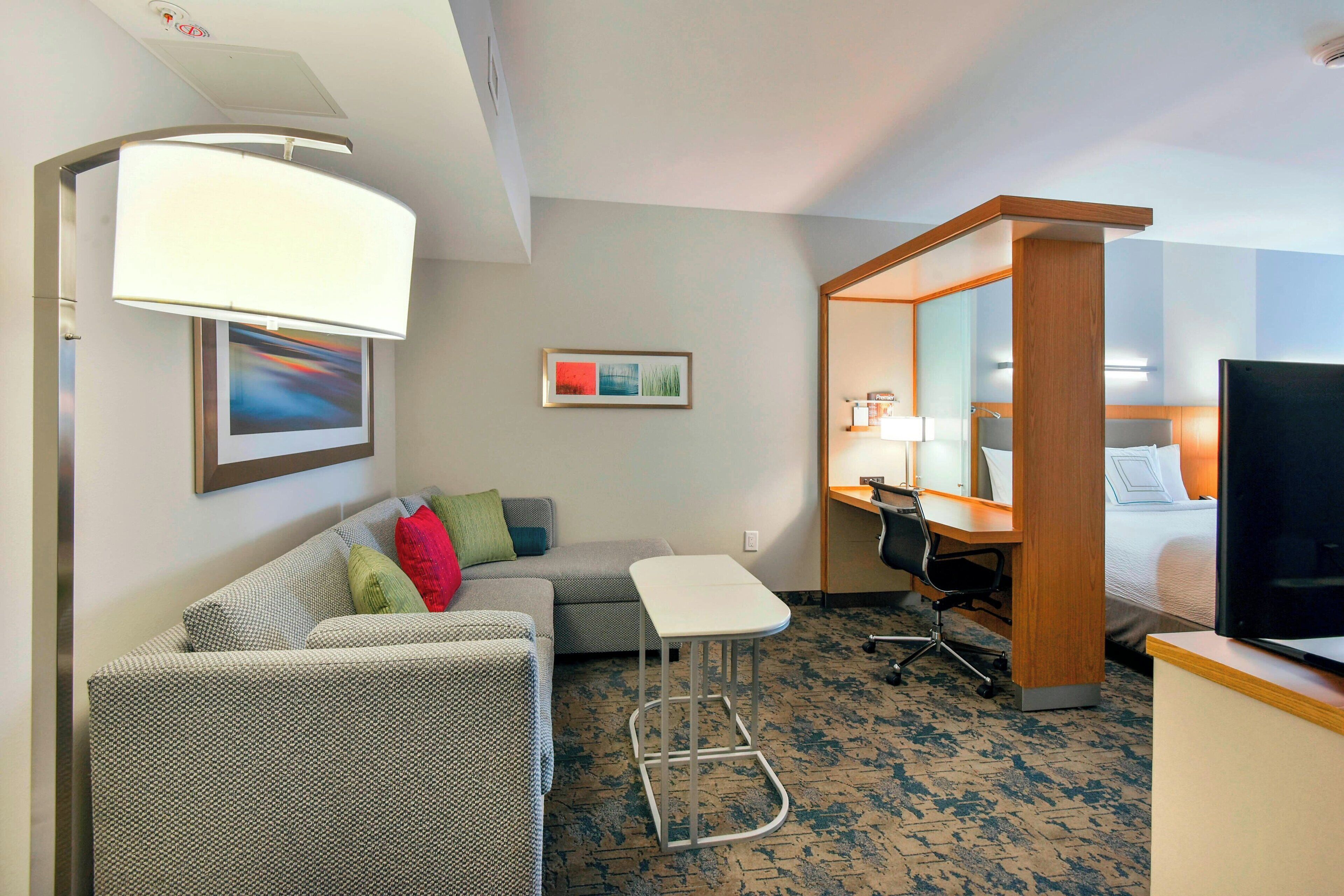 A hotel room with a sofa, a small desk, a chair, a television, and a bed.