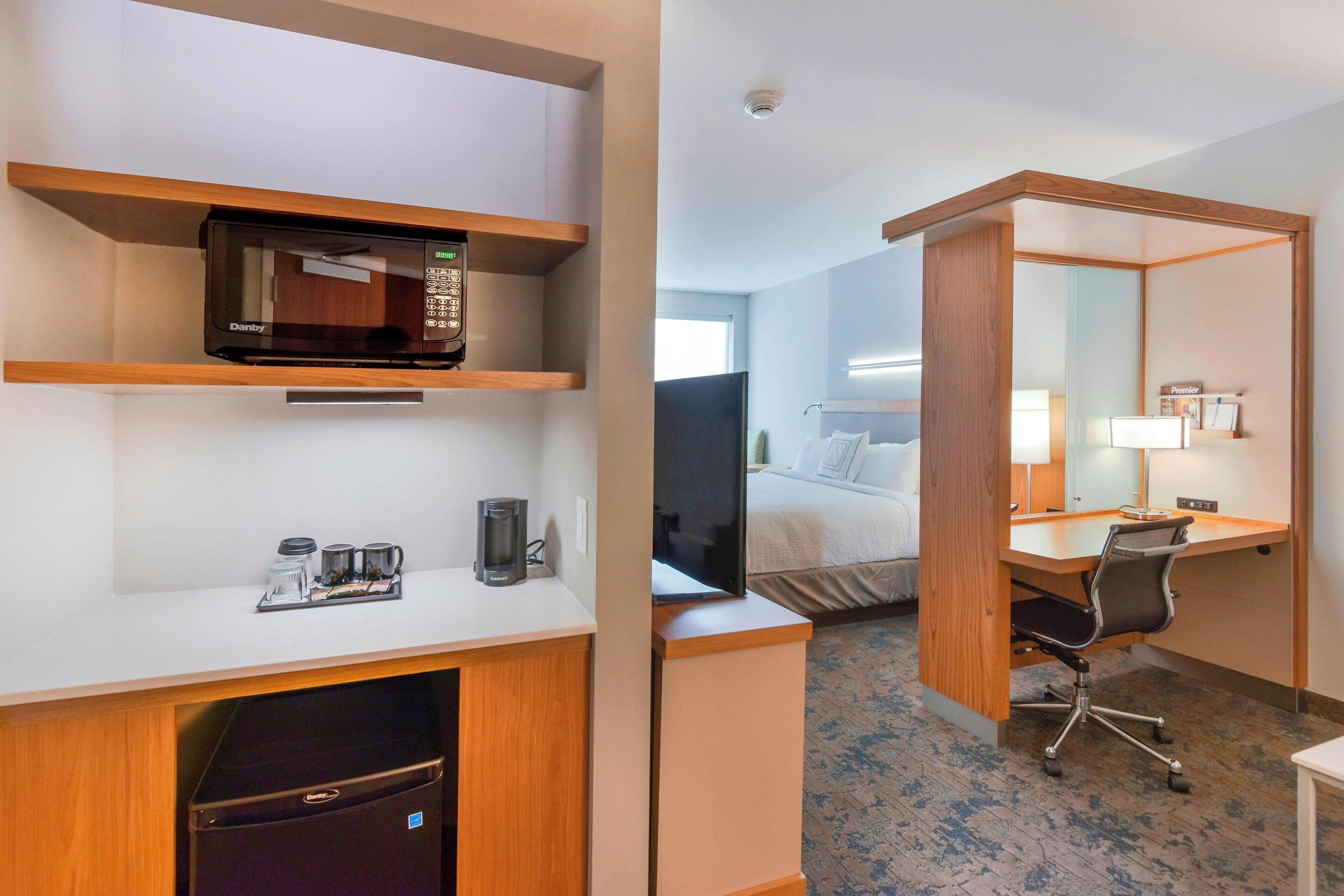 Habitación de hotel con microondas, cafetera y escritorio con silla.