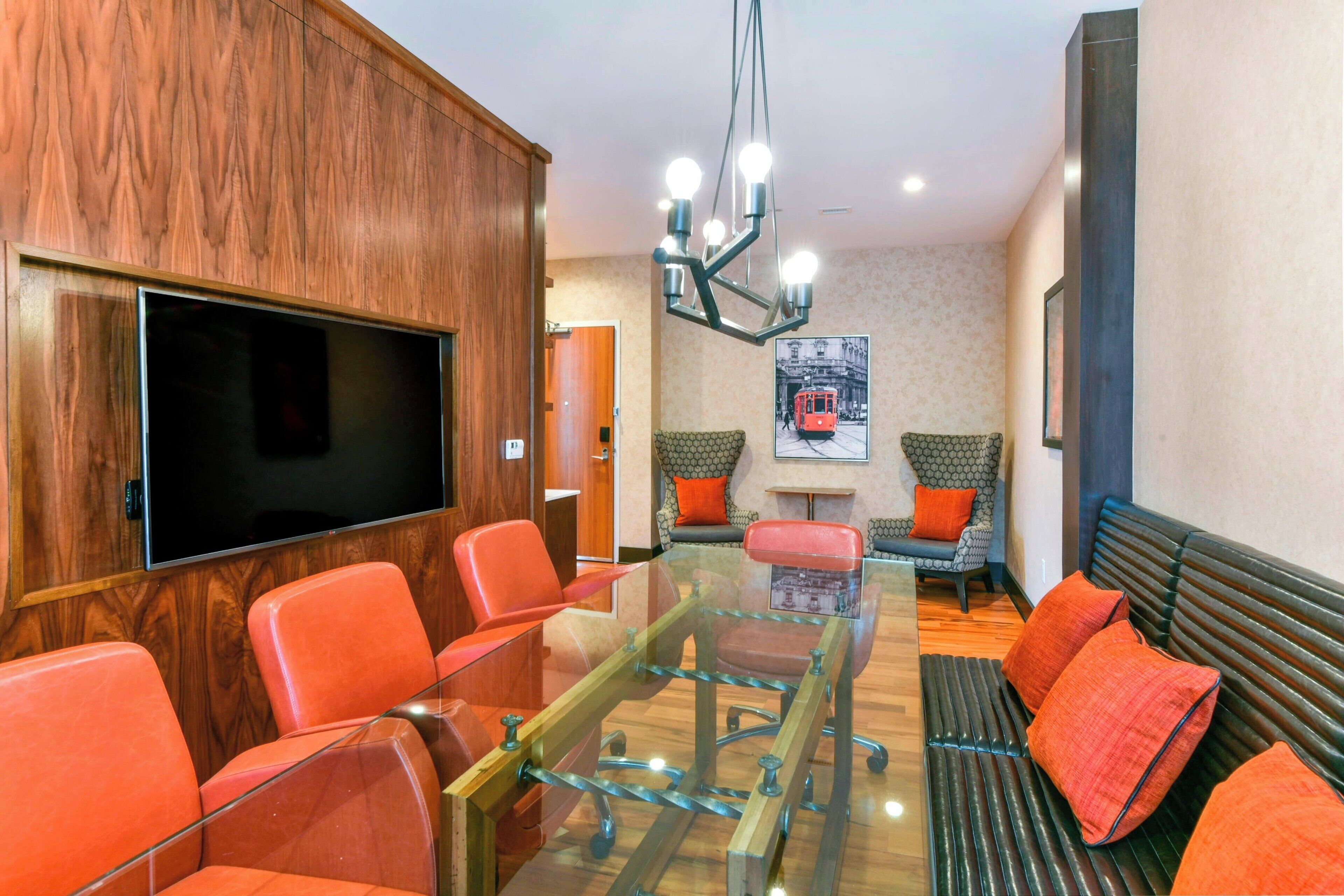 A modern conference room with a glass table, red chairs, a sofa, and a mounted TV.