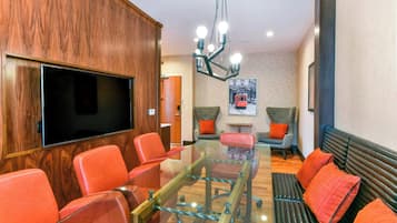 Una sala de conferencias moderna con una mesa de vidrio, sillas rojas, un sofá y un televisor montado.