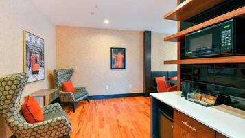 A modern living room with patterned armchairs, a wooden floor, a microwave, and a small table.