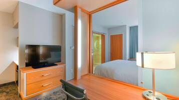 Una habitación de hotel con un escritorio de madera, televisión, espejo y lámpara de noche.