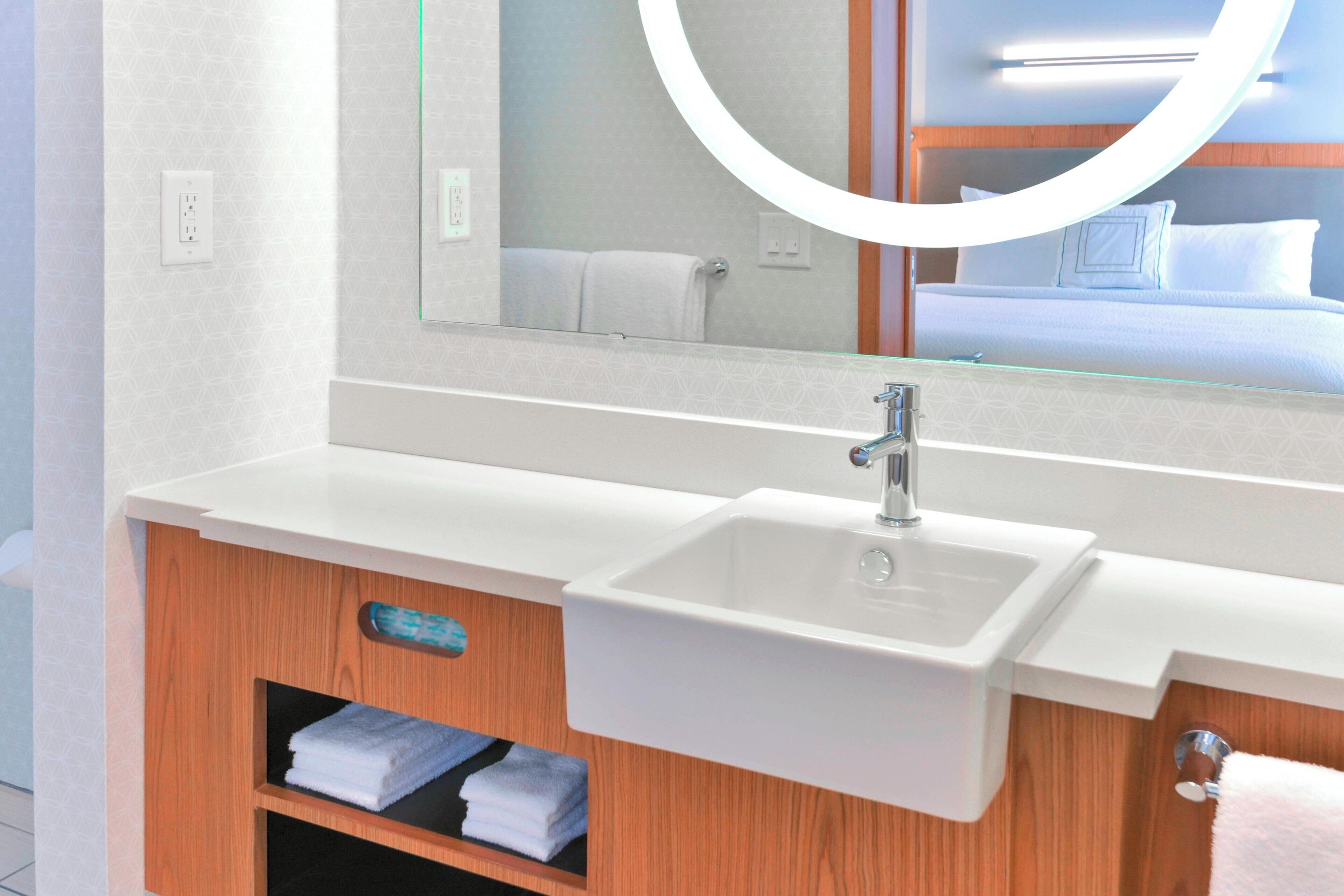 Un baño moderno con un lavabo blanco, tocador de madera y un espejo grande.