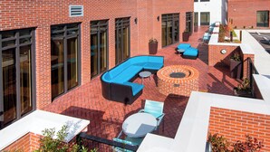 A courtyard with a brick wall, large windows, and outdoor seating including a blue sofa and round table.