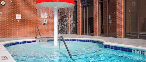 A swimming pool with a red and white water feature, surrounded by a brick building with large windows.