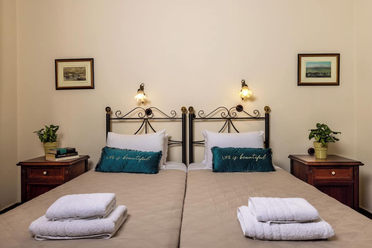A double bed with two pillows, a nightstand with a plant, and a framed picture on the wall.