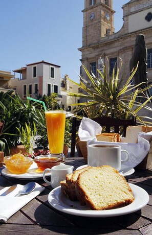 Una mesa con alimentos para el desayuno, como tostadas, un vaso de zumo de naranja y una taza de café, con una torre del reloj al fondo.