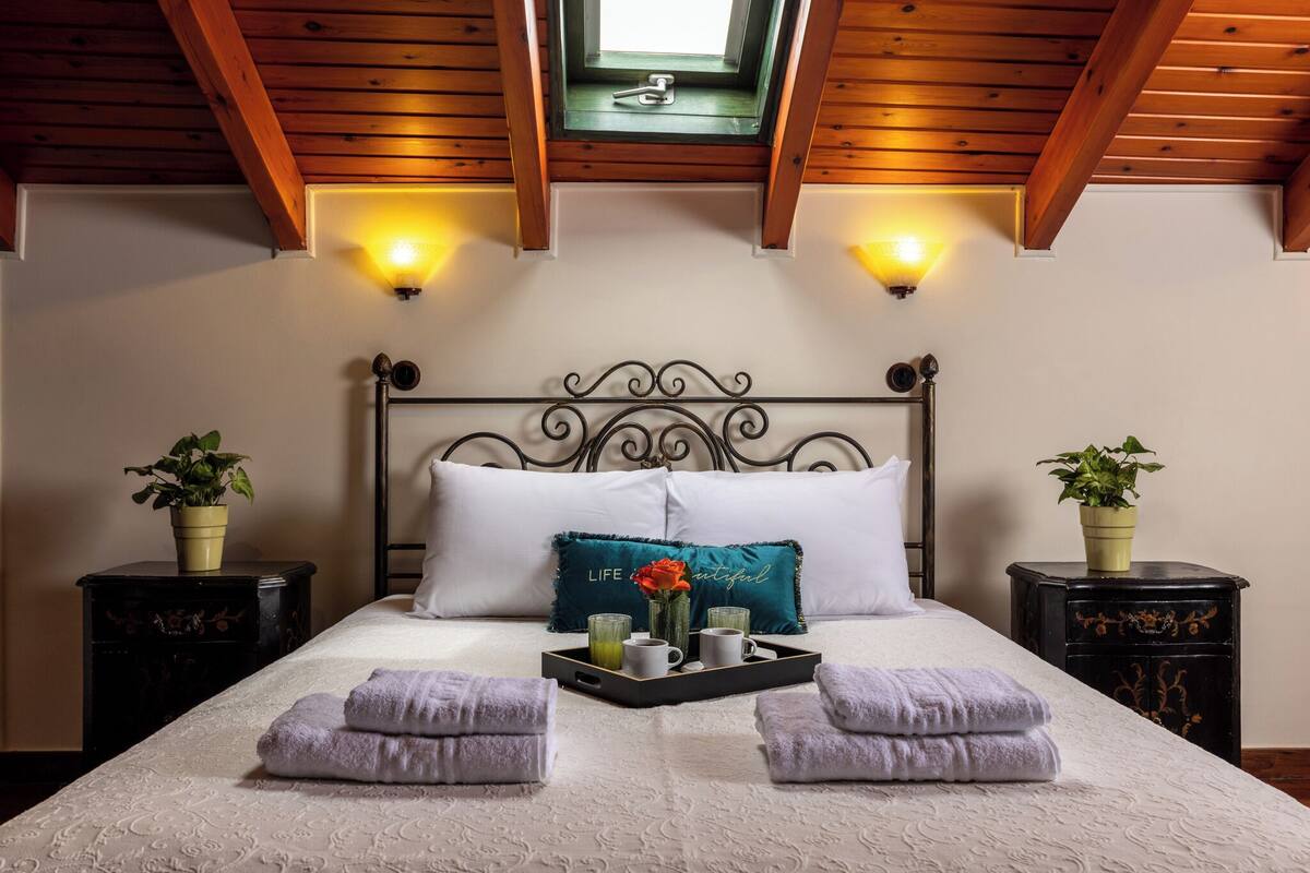 A neatly made bed with a tray of towels and a decorative pillow, a bedside plant, and a wall-mounted light fixture.