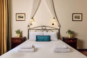 Una cama bien tendida con sábanas blancas, un almoháron teal con la frase 'LIFE is beautiful' y dos mesitas de noche con plantas en macetas.